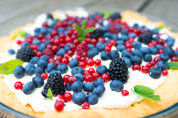 Tart with fresh blueberries, raspberries, blackberries, red currants and whipped cream decorated with mint leaves. View from above