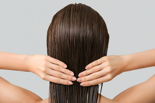Beautiful young woman after washing hair against grey background, back view