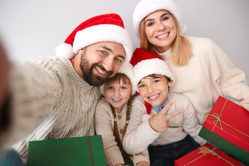 Happy family with Christmas gifts taking selfie on light background