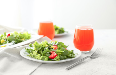 Plates with fresh tasty salad and glasses of juice on table