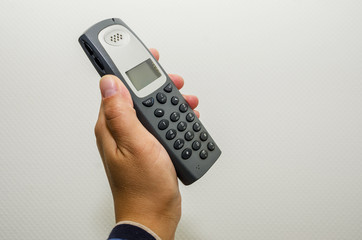 office cordless telephone in hand on wall background