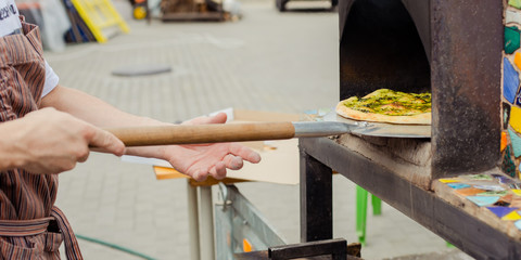 Baking pizza on a street Sunday market. Take out the finished pizza from the oven.