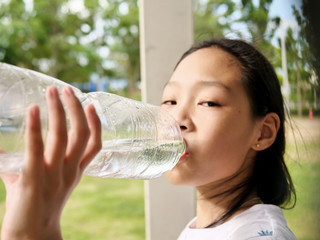 Asian girl drinking a bottle of water outdoor.