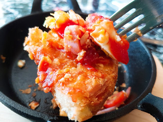 Pizza food, ham sausages, fried eggs, tomato sauce in a black pan.