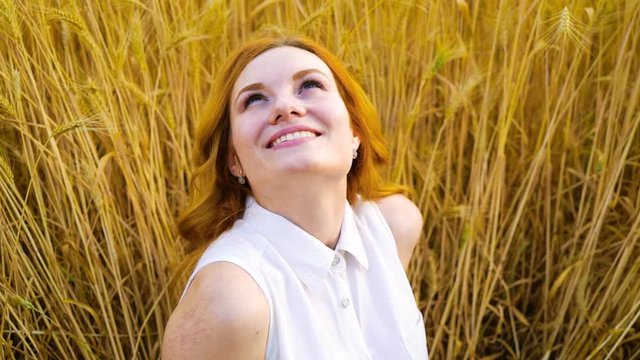 portrait of happy red haired woman looking up in the sky sitting in wheat field