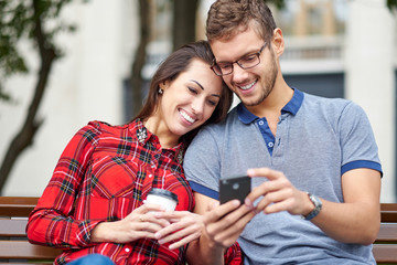 Happy couple with smart phone. Happy young loving couple standing outdoors together and looking at the mobile phone together