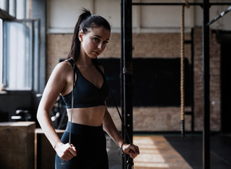 Fototapeta na wymiar Fit and healthy woman standing at gym with skipping rope. Sportswoman resting after workout.