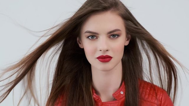 Portrait of a beautiful young woman with long brown hair. Stylish  girl in a red leather jacket with a red lips.