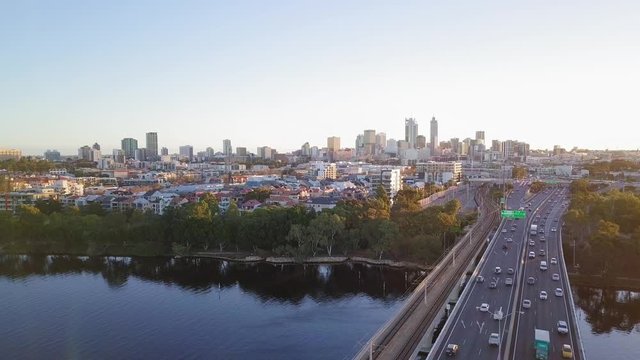 Aerial sideways motion over a bridge leading to Perth City in Western Australia. Cars going thorough the bridge at golden hour with view at the skyline.