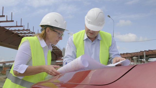 Male and female engineers are discussing a flyover construction project. Developers are working on project documentation at a construction site.