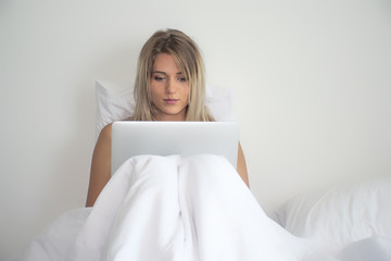 Happy beautiful woman working on a laptop sitting on the bed in morning.