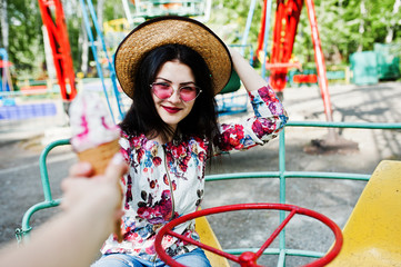 Portrait of brunette girl in pink glasses and hat with ice cream at amusement park.