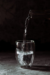 Water poured from the bottle into a glass cup on a black background
