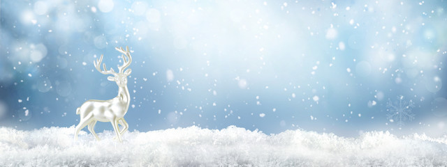 Christmas background with white decorative deer in snow on blue sky background in snowfall. Banner...