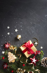 Christmas dark black background with beautiful texture and Golden gift box with red ribbon, fir branches, cones, Christmas tree toys stars, Christmas tree cookies, top view, copy space.