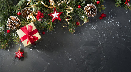 Christmas dark black background with beautiful texture and Golden gift box with red ribbon, serpentine, fir branches, cones, Christmas tree toys stars, top view, copy space.