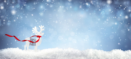 Christmas background with white decorative deer in snow on blue sky background in snowfall. Banner format, copy space.