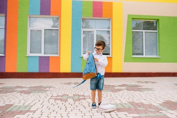 Back to school. Happy smiling boy in glasses is going to school for the first time. Child with backpack and book outdoors. Beginning of lessons. First day of fall.