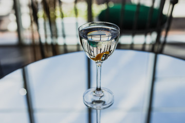 Obraz premium Dry martini cocktail with an orange twist in a nick and nora glass on a glass table with a reflection