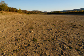 The bed of the dried-up river in the light of the setting sun, with clouds in the sky, with mountains in the background, shot during the season of golden autumn. Yellow-golden-brown.