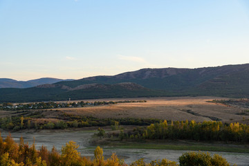 The bed of the dried-up river in the light of the setting sun, with clouds in the sky, with mountains in the background, shot during the season of golden autumn. Yellow-golden-brown.