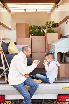 Father And Son Sitting On Tailgate Of Removal Truck Having Drink On Moving Day