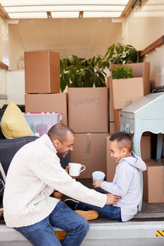 Father And Son Sitting On Tailgate Of Removal Truck Having Drink On Moving Day