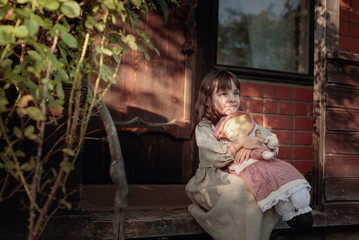 Girl with handmade doll on a summer evening near the old house.