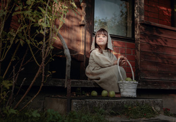Dreaming girl with apples on a summer evening near the old house.