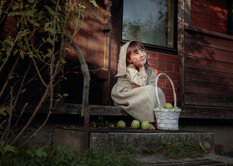 Dreaming girl with apples on a summer evening near the old house.