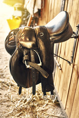 leather horse saddle in a stable hanging on the wall.