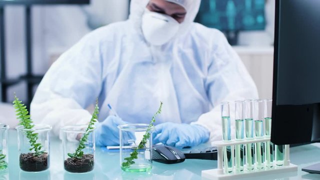 Close up footage of chemist desk with test sample plants. He grabs each of it and makes notes