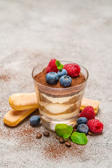 Classic tiramisu dessert with blueberries and raspberries and savoiardi cookies in a glass on concrete background