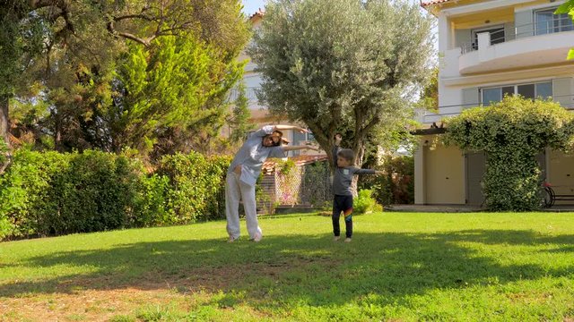 Grandmother with grandson doing sports on backyard, front yard. Cheerful grandmother having fun with grandson outdoor. Preschooler having fun with mother, grandmother. Smiling kid