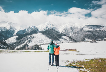 Loving couple standing and looking on beautiful snowy mountains peaks. Panoramic view. Back view.