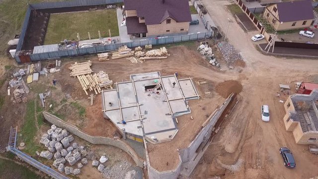 Aerial view of new modern cottage near the building site, construction materials and workers pouring concrete for the foundation. Clip. Process of new building construction.