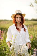 A redhead girl holding her hands in the pockets in the summer field