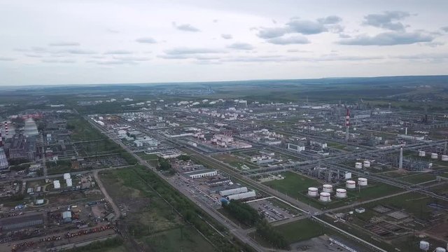 View from above of large industrial area located outside the city with fields and trees on the background against cloudy sky. Clip. Amazing view of factories tanks and tank farm.