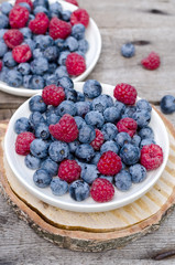Still life with a blueberries and raspberries on an old wooden table, at the garden. Rural natural food style.