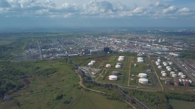 Aerial view of field with trees near the industrial area located outside the city. Clip. Amazing view of factories tanks and tank farm for bulk petroleum and gasoline storage