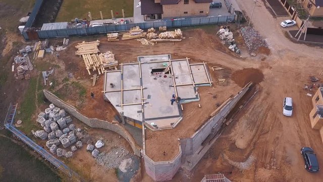 View from above of the construction site in progress, workers building new house or workshop and construction materials ( wooden boards, rocks, bricks). Clip. Process of new building construction.