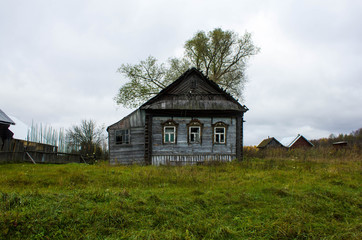 Naklejka na ściany i meble Old wooden house gray in a village in the Ivanovo region in Russia. The house, standing alone on a dull cloudy day in the hinterland of Russia.