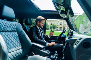 Obraz premium Handsome young businessman looking on his smart phone while sitting on the front seat