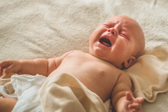Crying hungry newborn baby lying on the bed. Love baby. Newborn baby and mother.