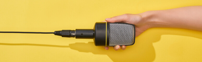 panoramic shot of woman holding microphone on yellow background