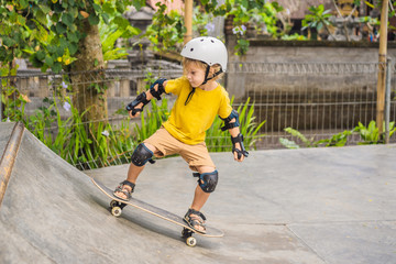 Athletic boy in helmet and knee pads learns to skateboard with in a skate park. Children education, sports