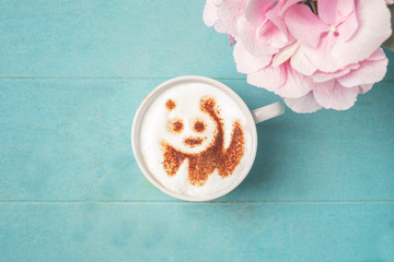White cup of coffee with panda pattern on the foam on a blue wooden background, top view, copy space.
