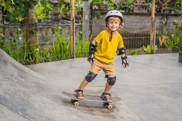 Athletic boy in helmet and knee pads learns to skateboard with in a skate park. Children education, sports © galitskaya