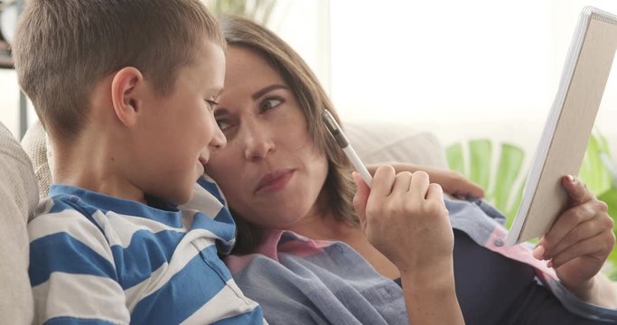Relaxed mother and son writing to do list in notepad at home