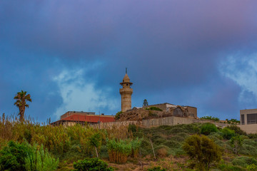 Fototapeta na wymiar European old lighthouse medieval building on green hill near Mediterranean waterfront in rainy cloudy weather time before storm 